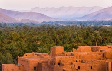 Traditonal adobe village with lush palm trees and Atlas Mountains in Morocco