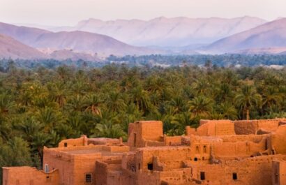 Traditonal adobe village with lush palm trees and Atlas Mountains in Morocco