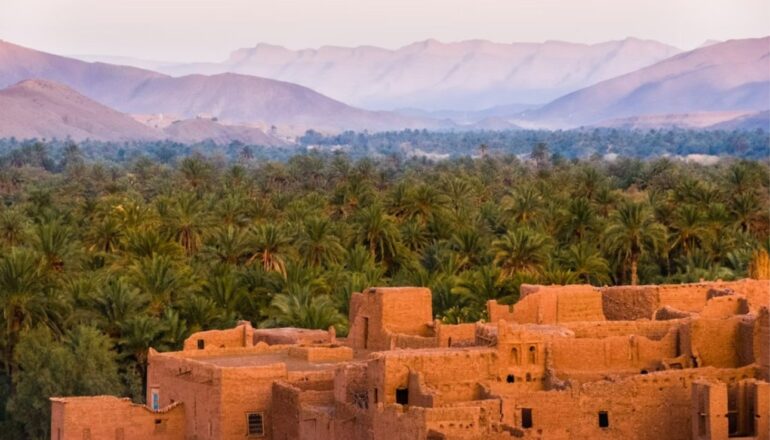Traditonal adobe village with lush palm trees and Atlas Mountains in Morocco