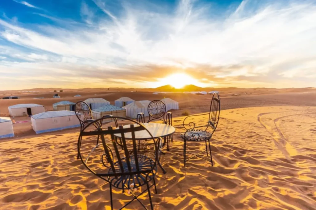 Sunset view over a luxury desert camp in Merzouga with table and chairs on golden sand dunes