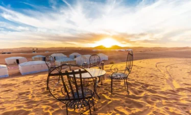 Sunset view over a luxury desert camp in Merzouga with table and chairs on golden sand dunes