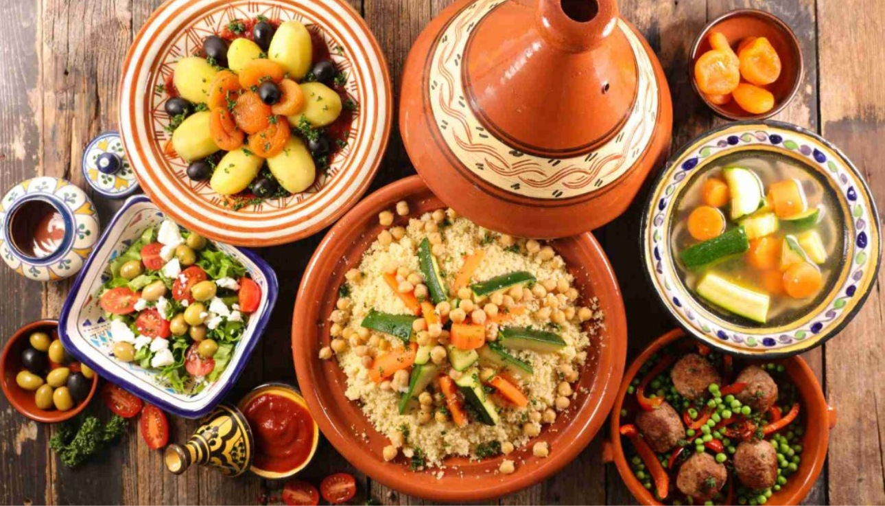 Traditional Moroccan couscous with vegetables , olives , kefta , and salads served in colorful ceramic dishes